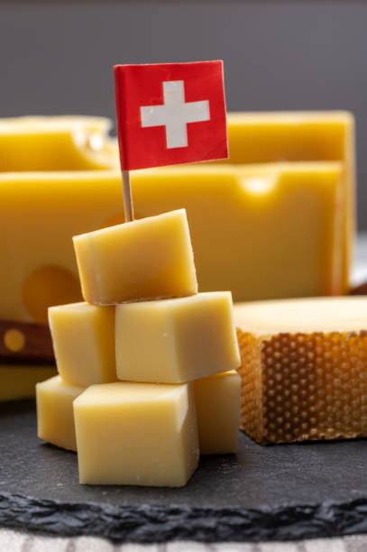 swiss cheeses, block of medium-hard yellow cheese emmental or emmentaler with round holes and matured gruyere served in cubes as mountain top with swiss flag. - cheese emmental cheese switzerland grated imagens e fotografias de stock