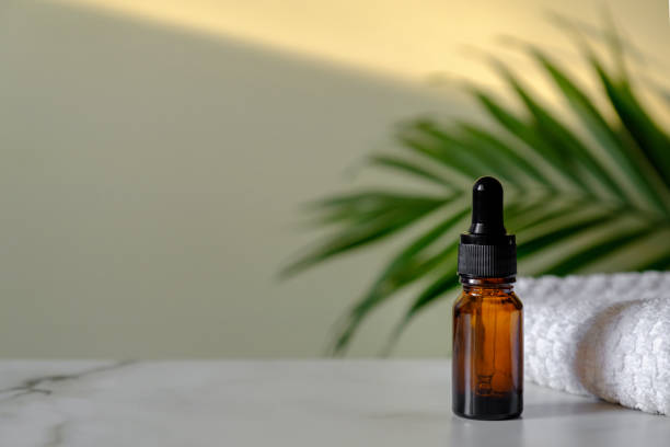 Essential oil bottle and towel on marble table, tropical palm leaf on background. Dropper bottle mockup for essential oil, serum, organic cosmetic products