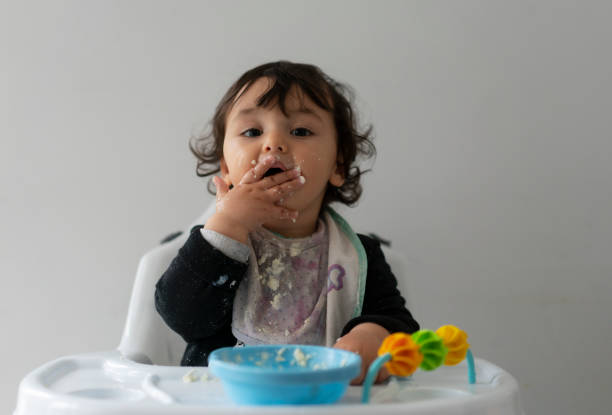 Cute baby boy in a mess learning self feeding, sitting in a high chair