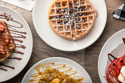Freshly baked Viennese waffles sprinkled with powdered sugar lying on a black ceramic plate on a wooden background.