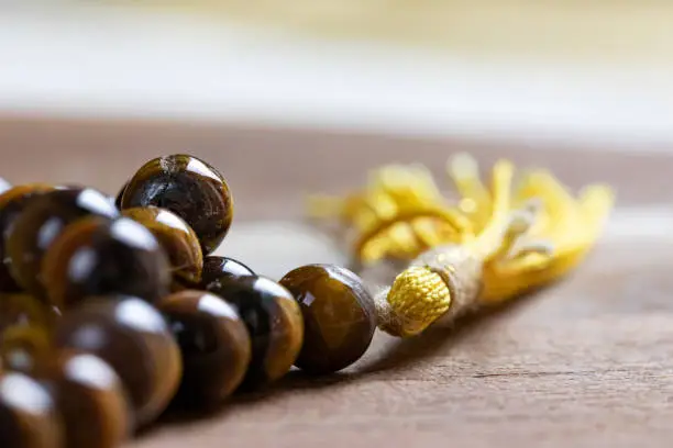Close up of a holy Mala prayer beads necklace made of tiger eye gem stones with a yellow tassel promoting mediation healing and peace