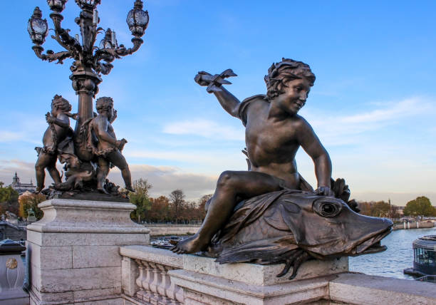 escultura na ponte. o garoto está sentado em um peixe, segurando um tridente. uma lanterna à distância. frança. paris. - estátua de bronze - fotografias e filmes do acervo