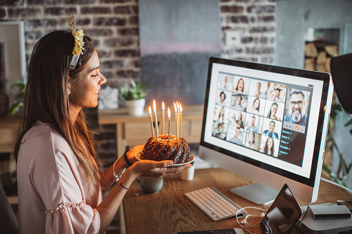 Teenage girl at home during pandemic isolation have birthday celebration and have video call with friends. She holding birthday cake with lighted candles