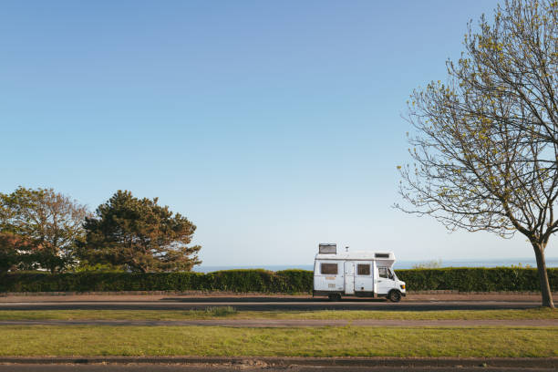 A vintage style camper van with a metal trunk attached to its roof parked on a seafront road with a grassed area in the foreground. There is copy space. A vintage style camper van with a metal trunk attached to its roof parked on a seafront road with a grassed area in the foreground. There is copy space. isle of thanet photos stock pictures, royalty-free photos & images