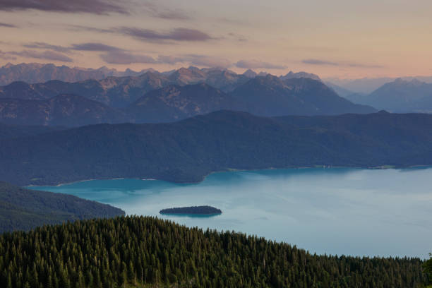 Turquoise coloured lake Walchensee with island Sassau during sunset, forest, mountains and clouds, Bavaria Germany