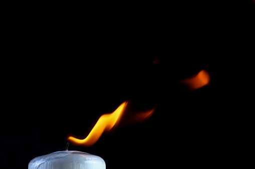 White candle burning with orange flame on black background.