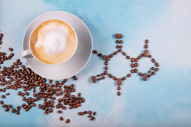 a cup of coffee with caffeine molecule created by coffee beans. a cup of coffee with caffeine molecule created by coffee beans. Chemical formula of Caffeine with roasted coffee spill out of cup on blue wooden background. caffeine molecule stock pictures, royalty-free photos & images