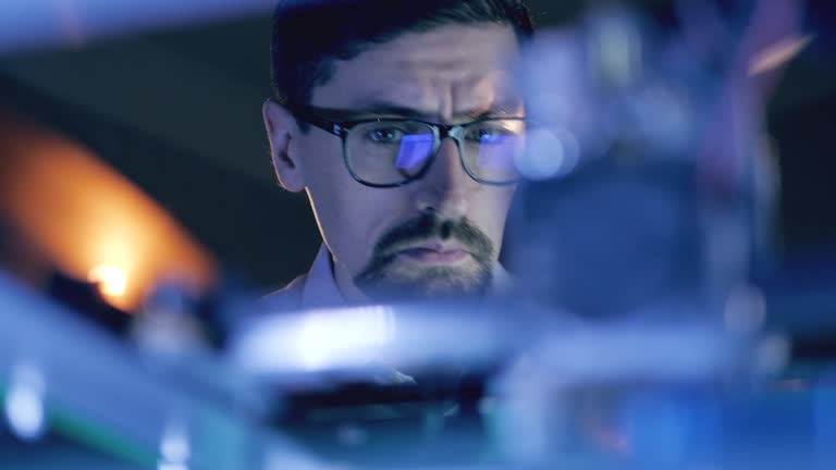 Man Working With A 3D Printer at 3d printing lab. Male specialist in glasses is observing a working mechanism