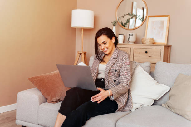 istock Young beautiful woman using a laptop computer at home, sitting on the sofa, smiling 1223517326