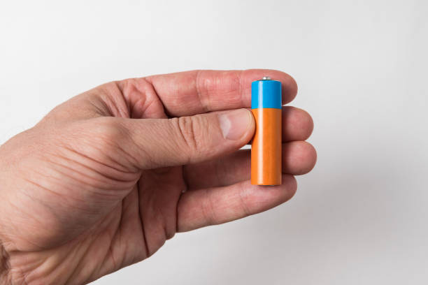 istock Man's hand holds a AA battery. Accumulator on white background 1223518311