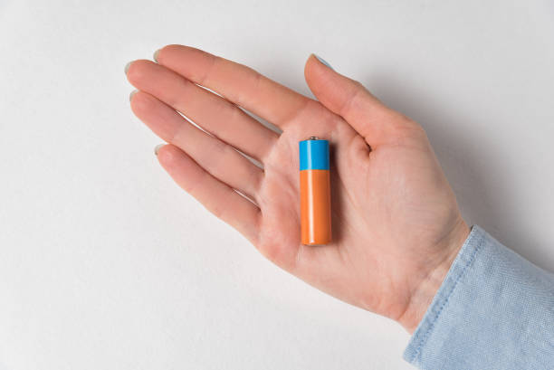 istock AA alkaline battery lying on the women's hand. Generic accumulator on white background 1223518325