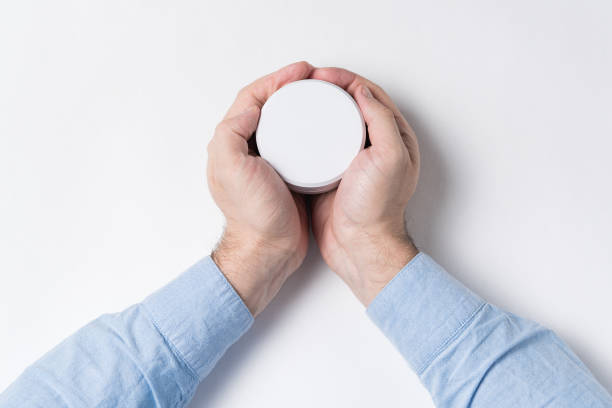 istock Male hands holding white cosmetic jar, mockup. White background, top view 1223519312