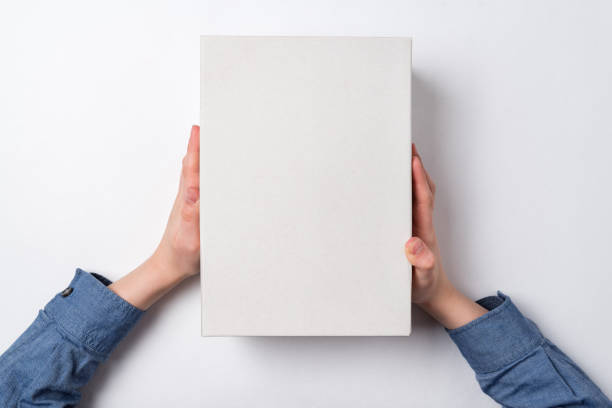 istock Children's hands holds white cardboard box on white background. Top view. Shipping concept. 1223519356