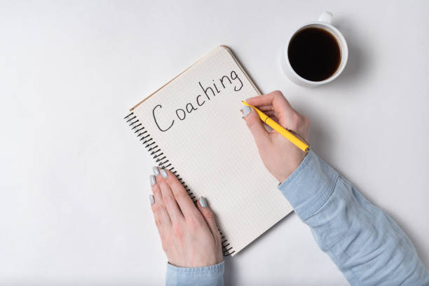 istock Notepad with word COACHING. Female hands and cup of coffee on white background. Top view 1223520962