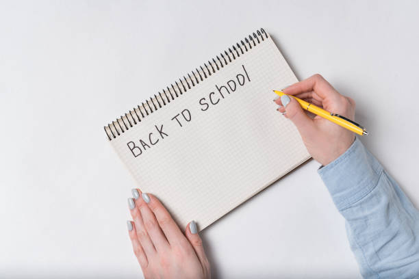 istock Female hand writes in notepad a words BACK TO SCHOOL. Top view 1223520973