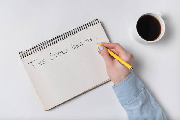 istock THE STORY BEGINS text in copybook. Female hands writing in Notepad. Coffee time. Handwritten text. 1223520978