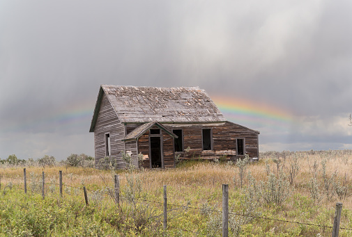 old dilapidated farmhouse under a grey sky with a rainbow