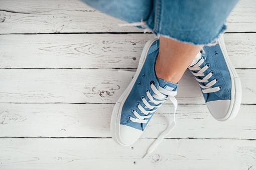 Teenager's feet in casual blue new sneakers on the white wooden floor close up image. Vintage style in modern fashion world concept image.