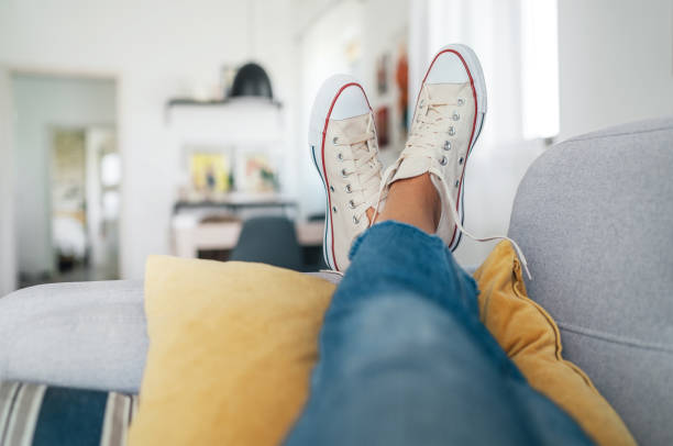 joven mujer acostada en nuevazapatillas beige hijo acogedor cómodo salón sofá poniendo los pies en almohadas y descansando y relajándose. concepto de ropa y calzado cómodo - eventos sociales despues del trabajo fotografías e imágenes de stock