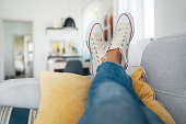 Young female lying in new beige sneaker son cozy comfortable living room sofa putting feet on pillows and resting and relaxing. Comfortable clothing and footwear concept