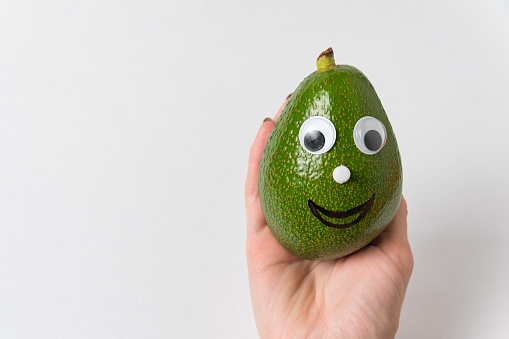 hand holding funny avocado with Googly eyes and smile. Healthy food concept.