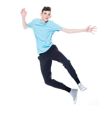 Front view of aged 12-13 years old caucasian teenage boys jumping in front of white background who is feeling joy