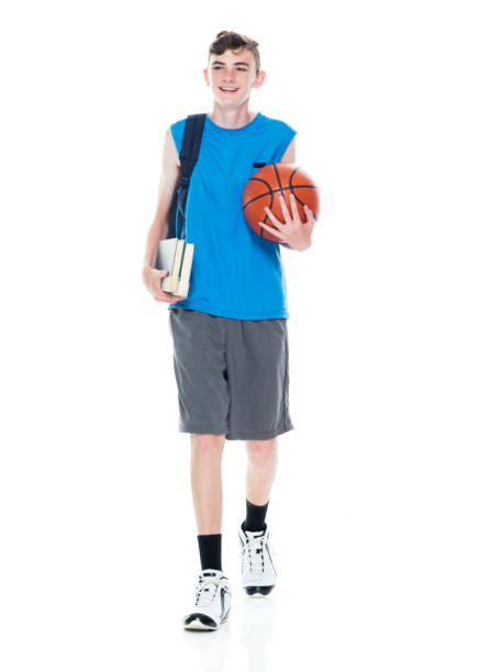 istock Caucasian male university student walking in front of white background wearing backpack and holding book and using sports ball 1223537611