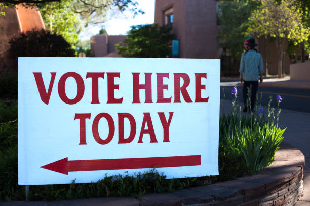 istock Man Walks Past VOTE HERE TODAY Sign 1223538515