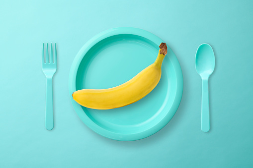 Overhead shot of plastic place setting with Banana on light blue background.
Diet concepts.