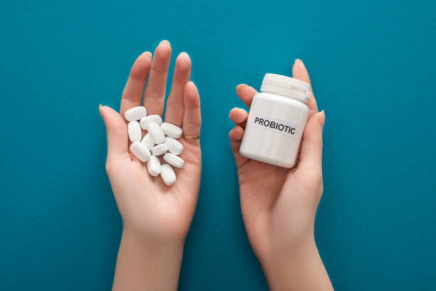 обрезанный вид женщины, держащей белый пробиотический контейнер и таблетки в руках на синем фоне - probiotics стоковые фото и изображения