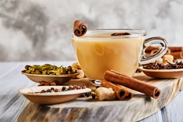Photo of Traditional Indian drink - masala tea with spices. Cinnamon, cardamom, anise, sugar, cloves, pepper on a light wooden background