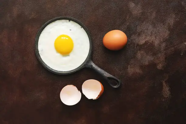 Photo of Fried egg in a pan, dark painted rustic background. Top view, flat lay, place for text.