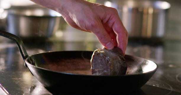 chef de mediana edad mezclando salsa de filete de carne frita con cuchara de madera en una sartén en la cocina de un restaurante - sales manager fotografías e imágenes de stock