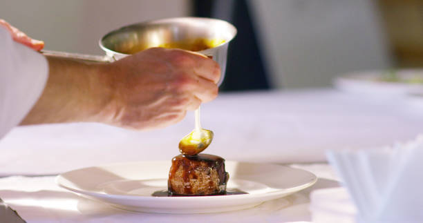 chef de mediana edad mezclando salsa de filete de carne frita con cuchara de madera en una sartén en la cocina de un restaurante - sales manager fotografías e imágenes de stock