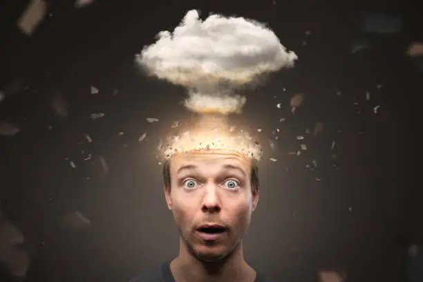 A man looking into the camera with a shocked expression. The top of his head is exploding in a non cruel way. A mushroom cloud is rising above the head.