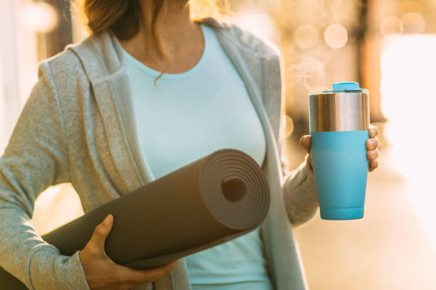 Woman headed to yoga with yoga mat and coffee cup stock photo