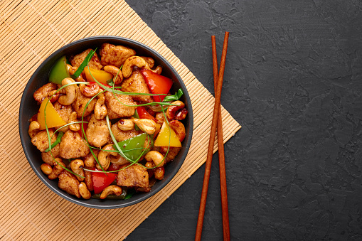 Gai Pad Med Mamuang or Thai Cashew Chicken in black bowl on dark slate backdrop. Kai Med Ma Muang is thai cuisine dish with chicken meat, capsicum, onion, scallions, chilli. Thai Food. Copy space