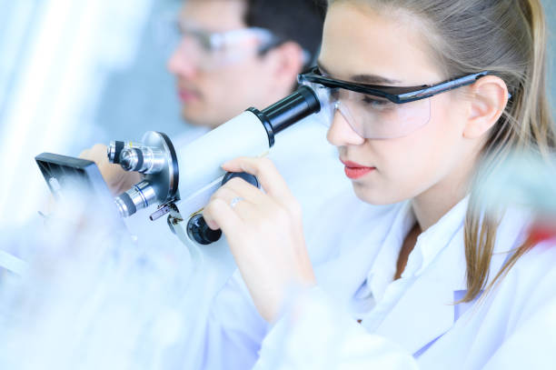 istock Young female scientist looking through microscope in laboratory, running an experiment or research. Medical healthcare technology, pharmaceutical research and development concept. 1223572484