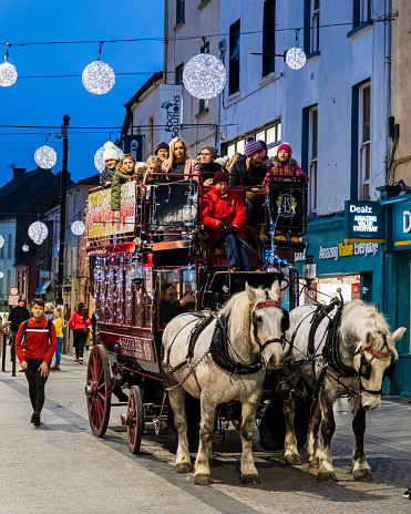 Horse-drawn carriage carrying people under Christmas decorations in downtown Waterford, a city in the south east of Ireland.