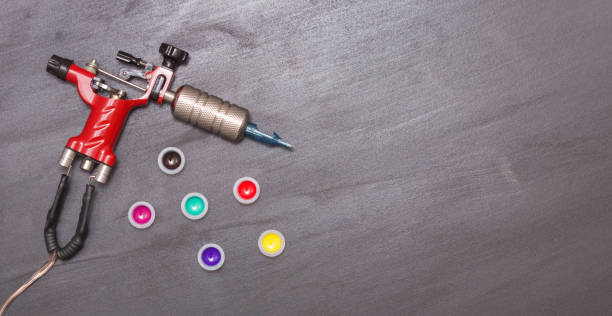 istock Rotary tattoo machine and disposable plastic jars with colored paints on a black background. Free space for text. Top view. Banner 1223580713