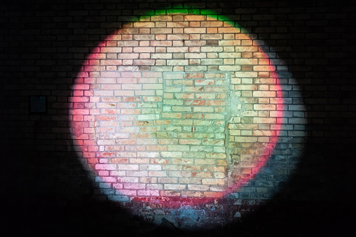 A colourful circle on a brick wall, copy space in the centre.\n\nNote: not a specific location, just playing with lights, trying to get a specific colour scheme.