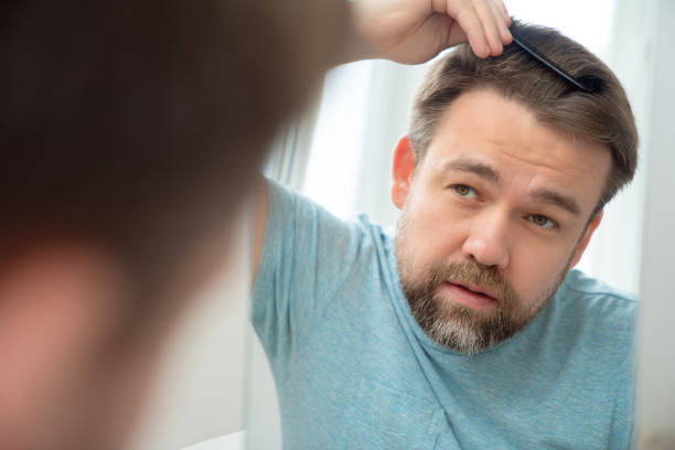 istock man combs hair and beard looking in mirror. 1223581666
