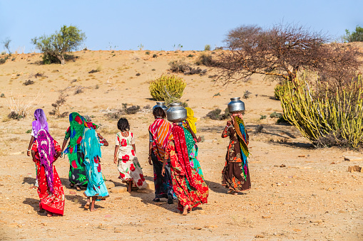 Indian little girls crossing sand dunes and carrying on their heads water from local well, Thar Desert, Rajasthan, India. Rajasthani women and children often walk long distances through the desert to bring back jugs of water that they carry on their heads.