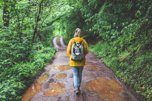 istock Woman in raincoat walking alone on county road 1223586975