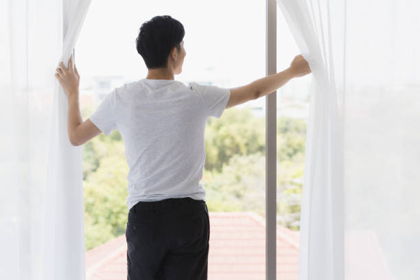 istock Man open the curtain and look outside the window. 1223588608