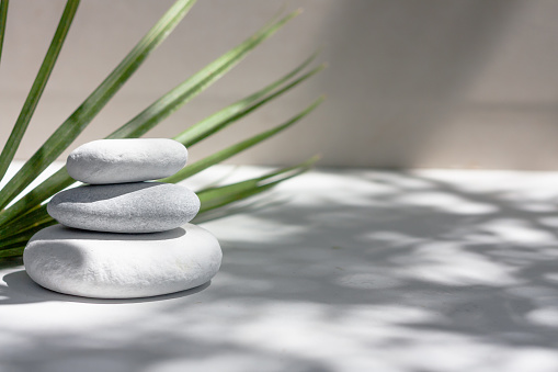 Three grey roundstones and bath towels on white background with green leaves. Spa stones, zen like concept.