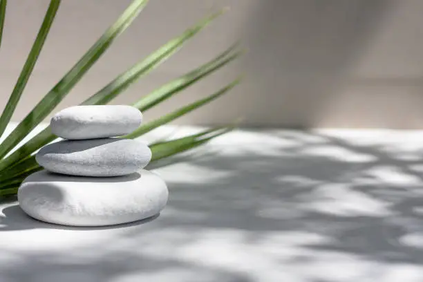 Photo of Three grey roundstones and bath towels on white background with green leaves. Spa stones, zen like concept.
