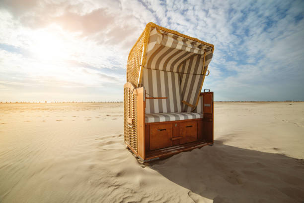 Typical roofed wicker hooded beach chairs in blue-white stripes on white sandy german north sea beach under beautiful blue summer skyscape at the beach of St. Peter-Ording, Nordfriesland, Germany.