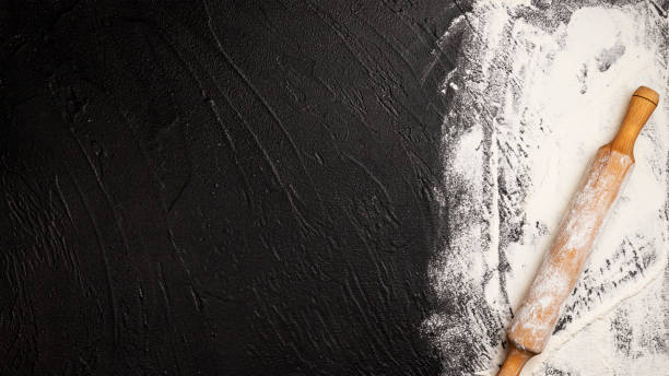 istock Sprinkled wheat flour and wooden rolling pin on black background 1223592629