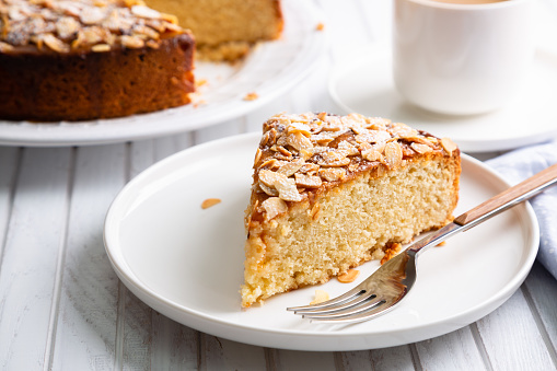 Almond and lemon cake with sliced almonds topping and a coffee cup on a white wooden table